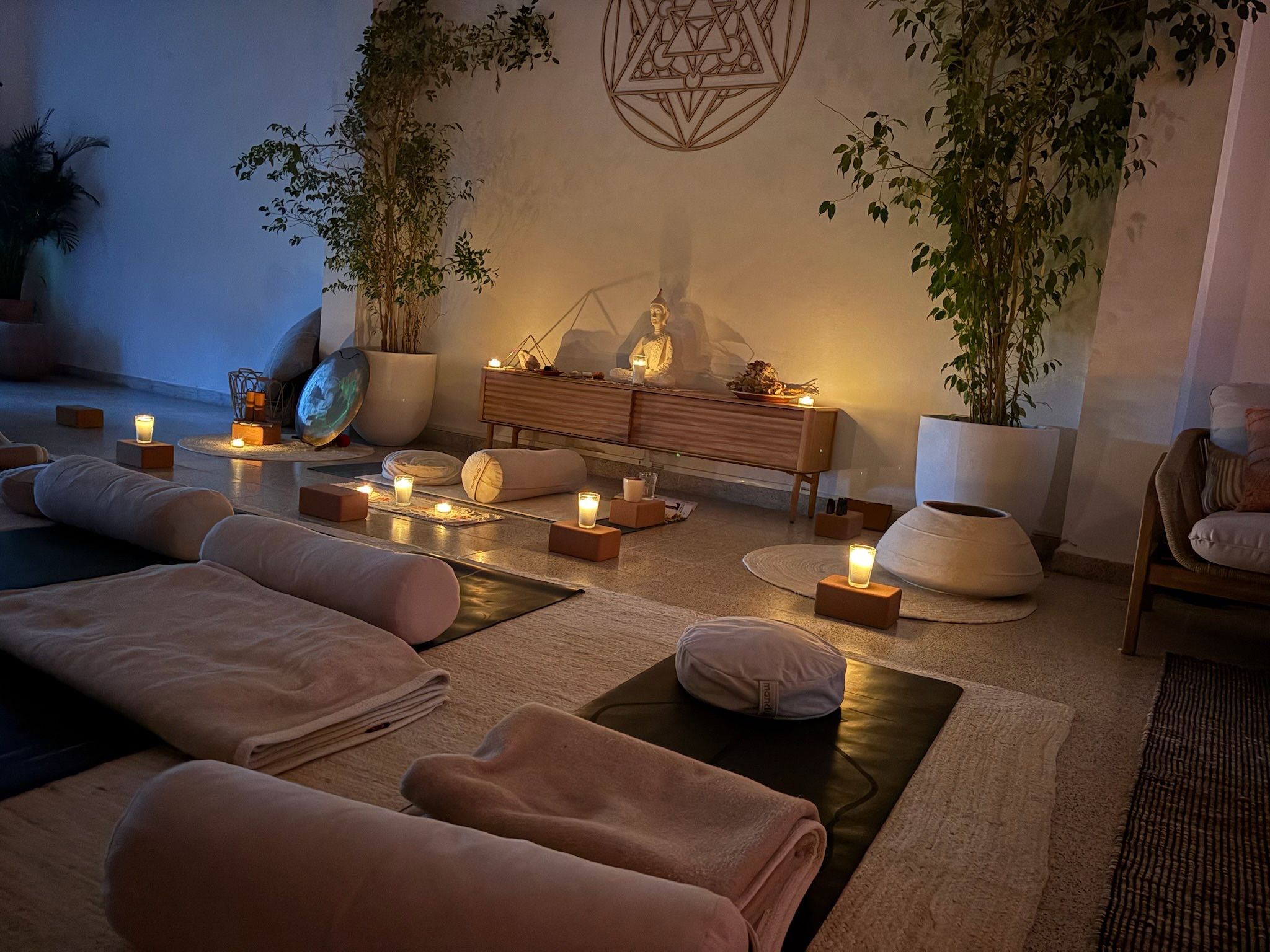 O espaço de eventos ao anoitecer, com velas, almofadas e mantas dispostas sob um emblema de geometria sagrada