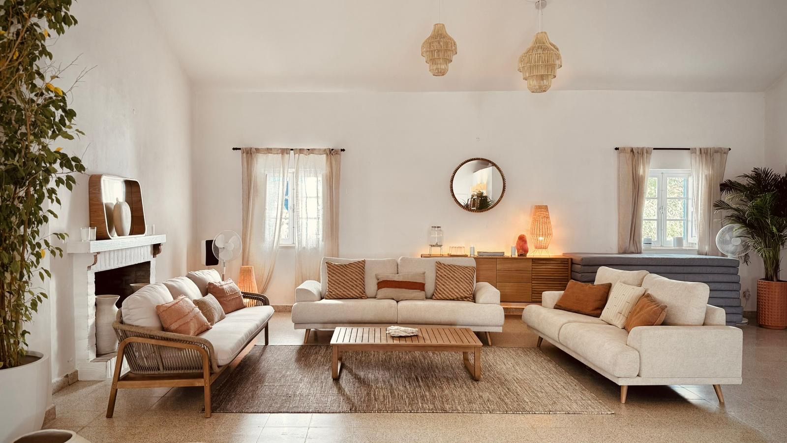 Uma sala de estar luminosa com sofás de linho, uma mesa de centro de madeira, candeeiros de rattan e uma lareira branca