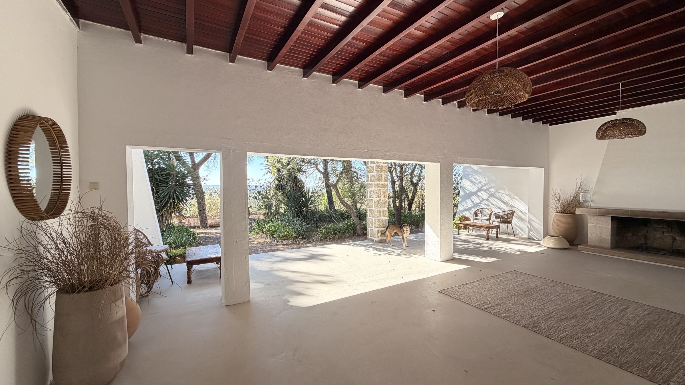 A shala Silencio: uma sala branca com teto de madeira escura, uma lareira e grandes aberturas para o jardim, com um cão deitado ao sol